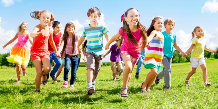 Laufende Kinder auf einer grünen Wiese. Die Kinder halten sich anden Händen.
