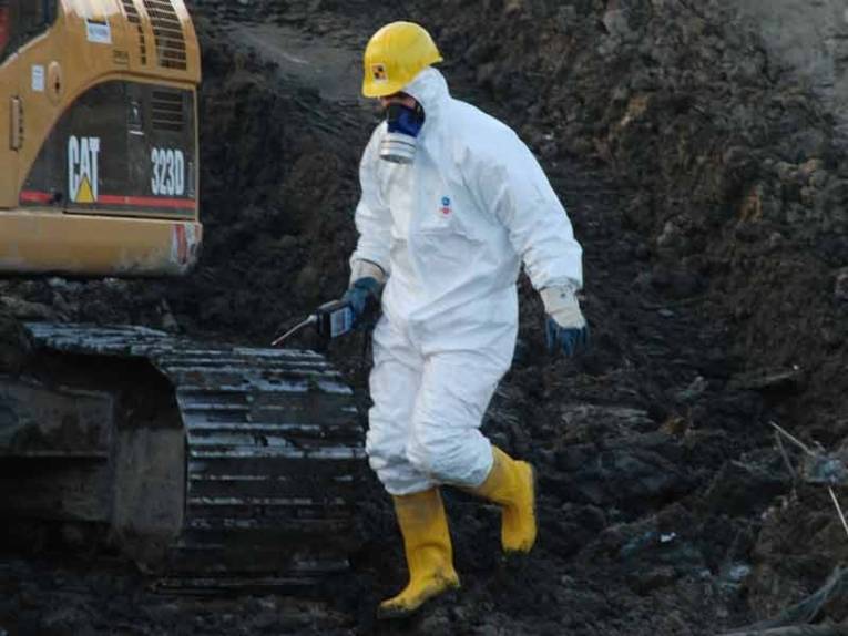 Person in einem weissen Arbeitsschutzanzug mit Atemmaske, gelbem Helm und gelben Gummistiefeln