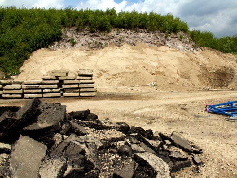 Ein bewachsener Sandhügel, Im Vordergrund Platten und abgetragene Teerklumpen.