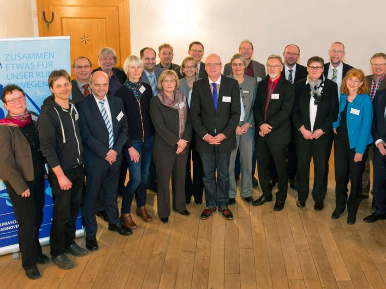 Zu sehen sind 20 Personen einer 26-köpfige Gruppe, die sich in Zweier- bzw. Dreierreihen im Halbkreis aufgestellt hat.