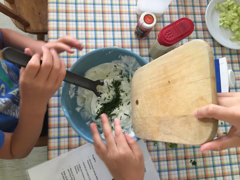 Ein Tisch mit einer Sch&uuml;ssel, einem Rezept, diversen Zutaten. Kinderh&auml;nde, die die Zutaten in die Sch&uuml;ssel geben und mit einem L&ouml;ffel verr&uuml;hren