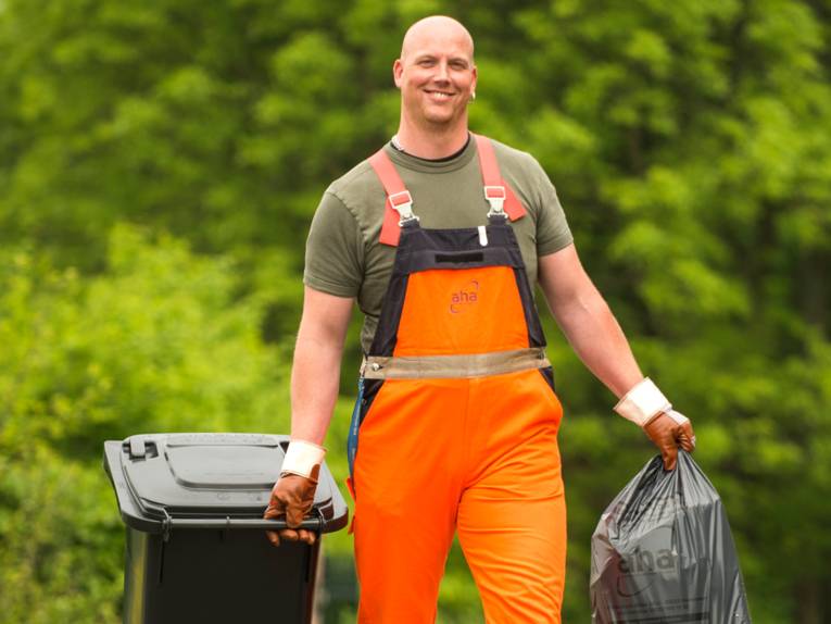 Ein Mitarbeiter der Abfallwirtschaft Region Hannover (aha) bewegt einen Restabfallsack und eine Restabfalltonne.