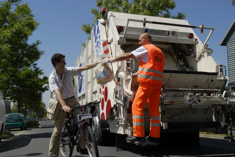 Fahrradfahrer reicht eine Mülltüte einem Mitarbeiter der Müllabfuhr