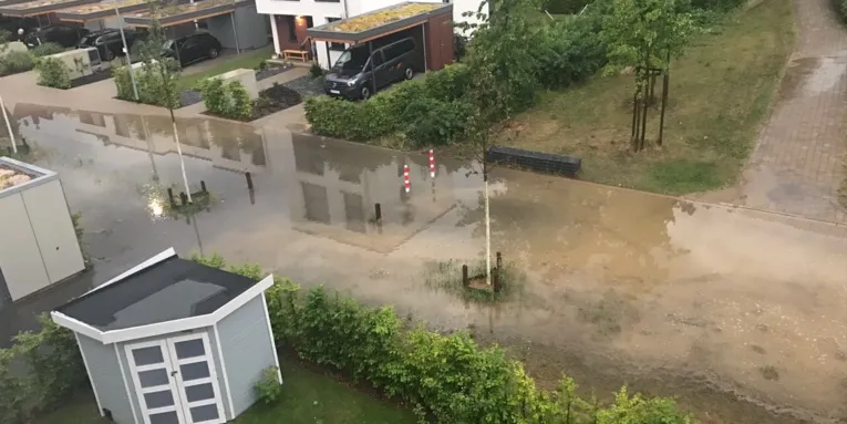Grundstückseinfahrten, Teile einer Straße und eines geflasterten Fussweges, die nach einen Starkregen unter Wasser stehen