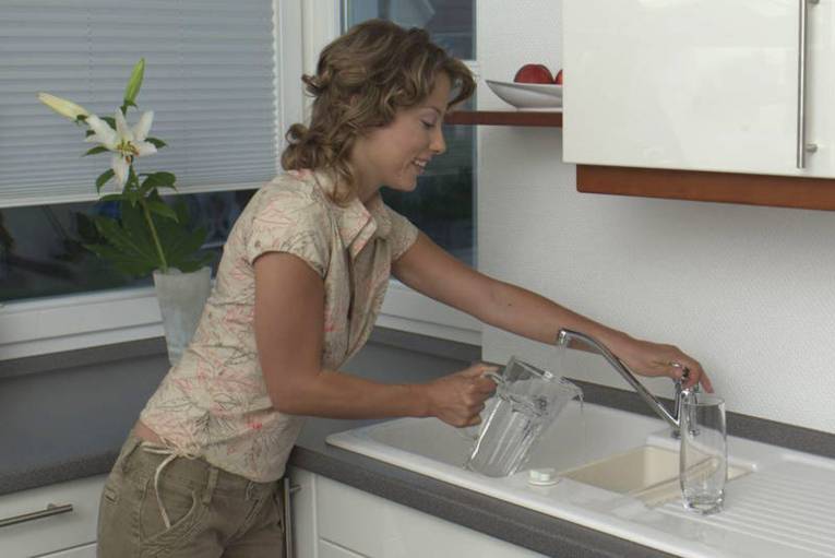 Ein Frau füllt Wasser aus der Leitung in eine Glaskaraffe