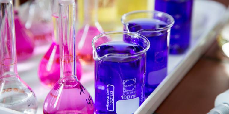 Kolbengefäße mit schmalem Hals (links) und zylindrische Becher mit Ausguss (rechts). Die enthaltenen Flüssigkeiten sind in den Farben Rosa (Messkolben) und Blau (Bechergläser) eingefärbt. 