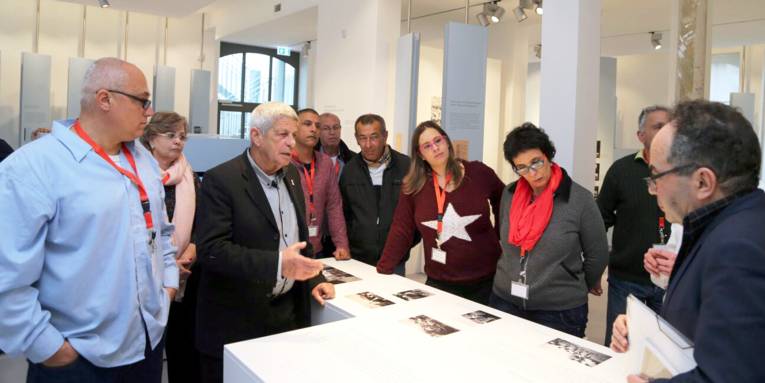 Zehn Personen schauen auf Ausstellungsstücke in der Gedenkstätte Ahlem