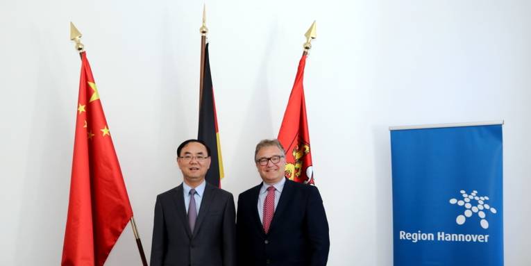 Zwei Männer stehen nebeneinander vor Fahnen.