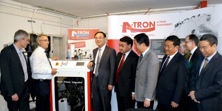 Acht Männer, darunter rechts die sechs Teilnehmer der Delegation, stehen an einem Blockheizkraftwerk.