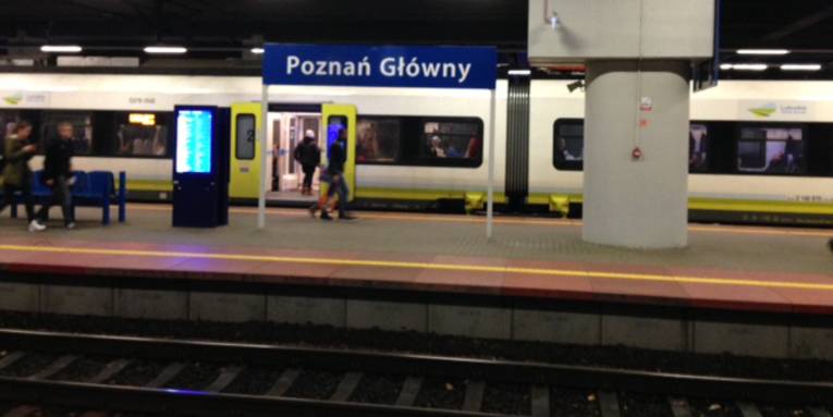 Ein Zug hält an einem Bahnsteig, auf dem Bahnhofsschild steht "Poznań Główny"