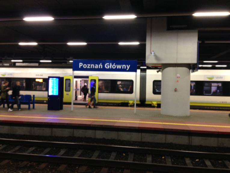 Ein Zug hält an einem Bahnsteig, auf dem Bahnhofsschild steht "Poznań Główny"