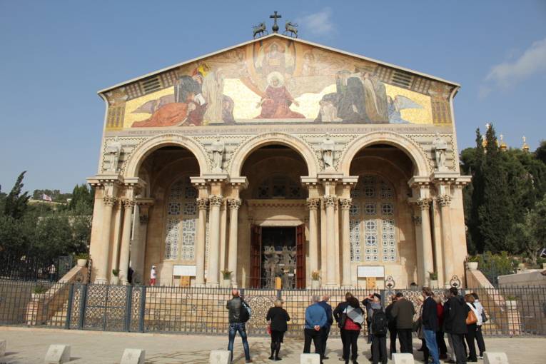 Eine Gruppe von Personen vor einer Kirche, deren Eingangsportal mit Säulen und einem Gemälde gestaltet ist.