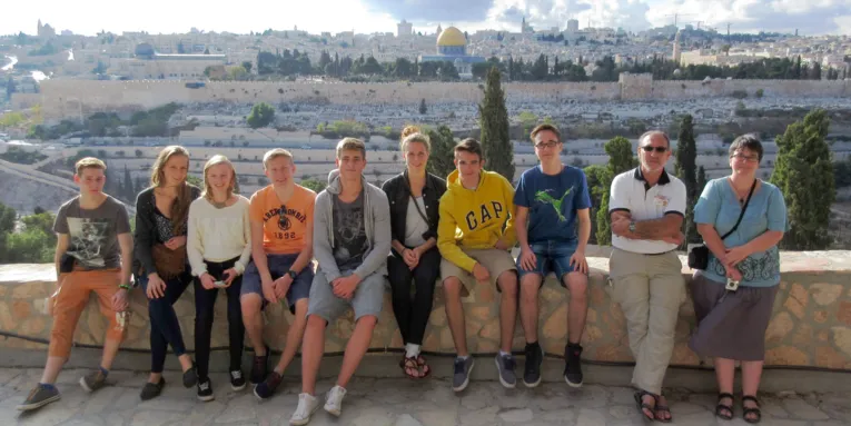 Zehn Personen sitzen auf einer Mauer, im Hintergrund sind Gebäude der Stadt Jerusalem zu sehen.