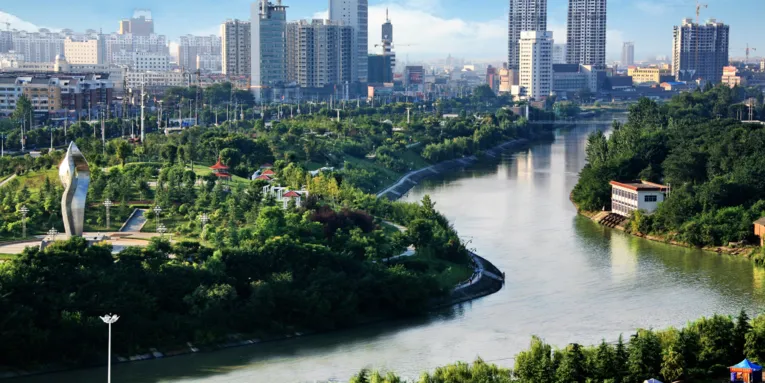 Chinesische Stadt mit einem Fluss im Vordergrund.