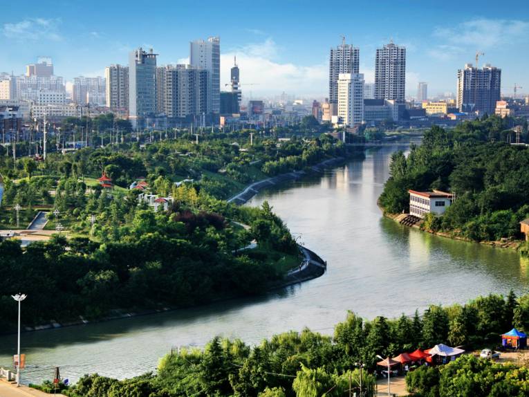 Chinesische Stadt mit einem Fluss im Vordergrund.