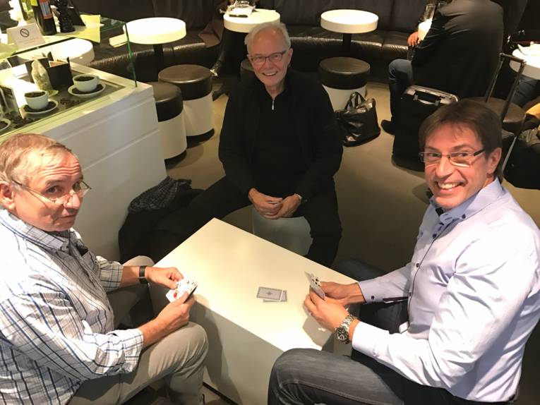 Drei Männer sitzen an einem Tisch und spielen ein Kartenspiel.