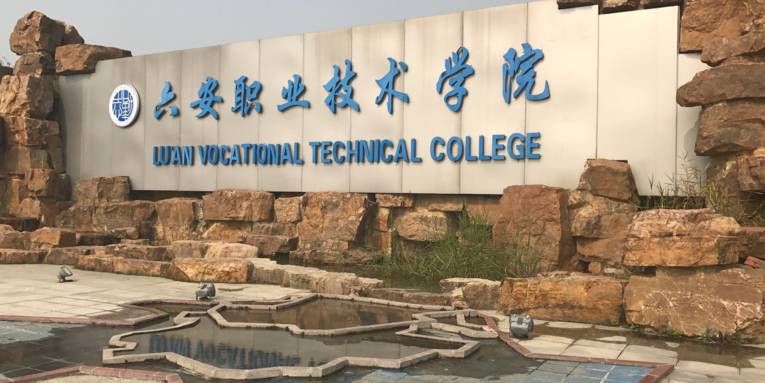 Das Schild des Vocational Technical College von Lu'an ist in eine Mauer aus Naturstein eingelassen, Scheinwerfer stehen davor, um es nachts anzustrahlen.