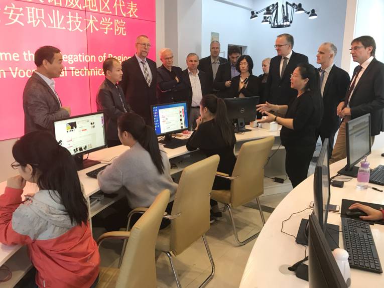 Schülerinnen sitzen an Computerbildschirmen, Teilnehmende der Delegation schauen ihnen beim Arbeiten am PC zu.