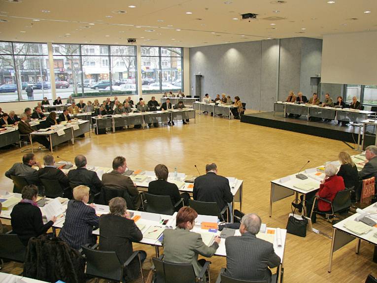 Mitglieder der Regionsversammlung sitzen auf Stühlen und an Tischen, die kreisförmig aufgestellt sind.