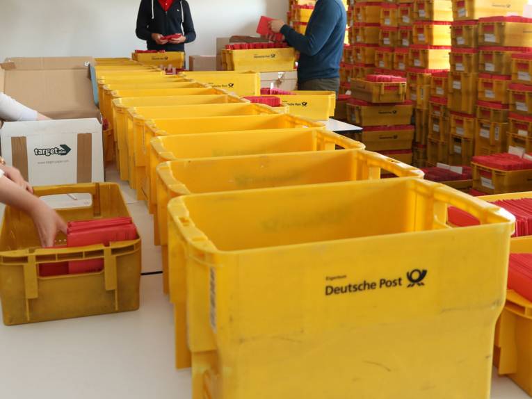 Mehrere gelbe Kisten mit geschlossenen roten Wahlbriefumschlägen.