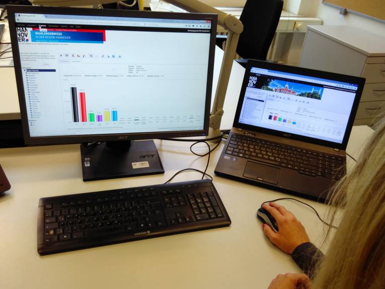 Eine Frau schaut sich Wahlergebnisse an einem Laptop und einem Bildschirm an.