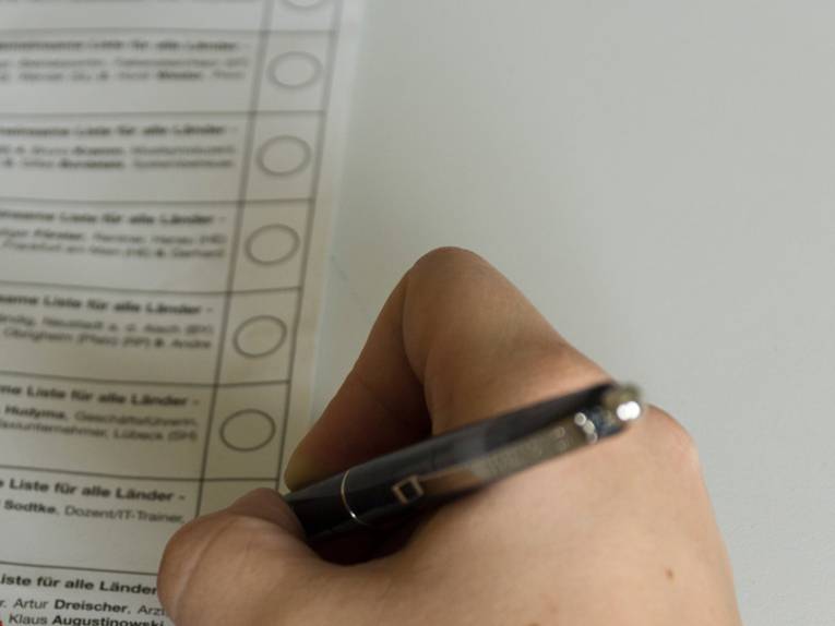 Die Hand einer Person, die gerade mit einem Kugelschreiber ihr Kreuz auf einem Stimmzettel setzen möchte. 