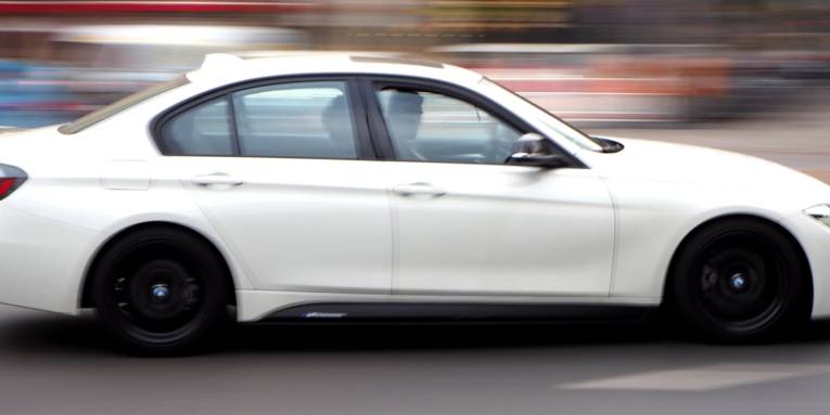 Ein weißes Auto fährt auf einer Straße. Durch die Bewegung ist der Hintergrund unscharf.