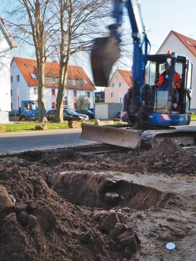 Zwei Bauarbeiter arbeiten mit einem Bagger an einer Straße.