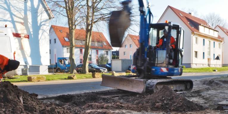 Zwei Bauarbeiter arbeiten mit einem Bagger an einer Straße.