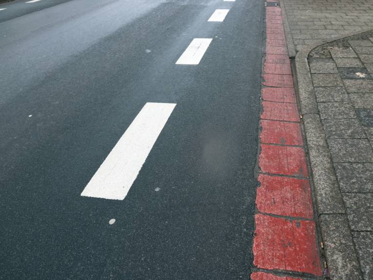 Eine weiße, gestrichelte Linie trennt auf einer Straße einen Bereich für Radfahrende ab.