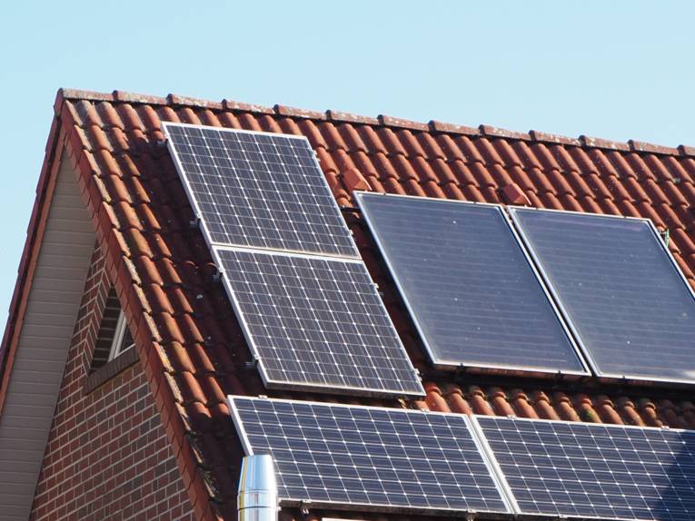 Photovoltaikmodule für Strom (links und unten) und Solarthermie für Wärme sind auf einem Hausdach montiert.