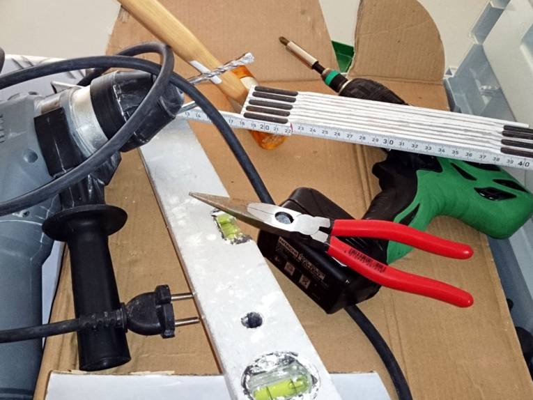 In einem Karton liegen verschiedene Werkzeuge, darunter Bohrmaschine, Zange, Wasserwaage, Akkuschrauber.