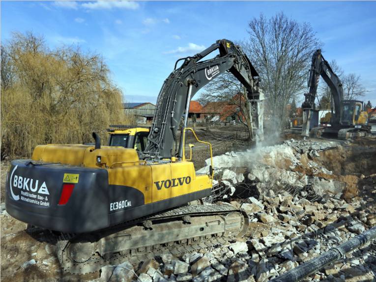 Zwei Raupenbagger bearbeiten mit Presslufthämmern die Trümmerteile einer Brücke.