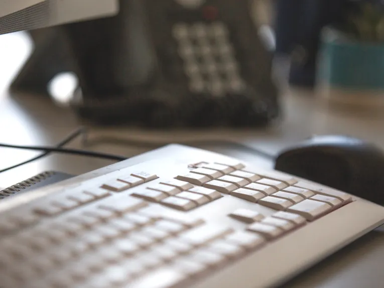 Blick auf ein Telefon, vorbei an einer Computertastatur und Computermaus.