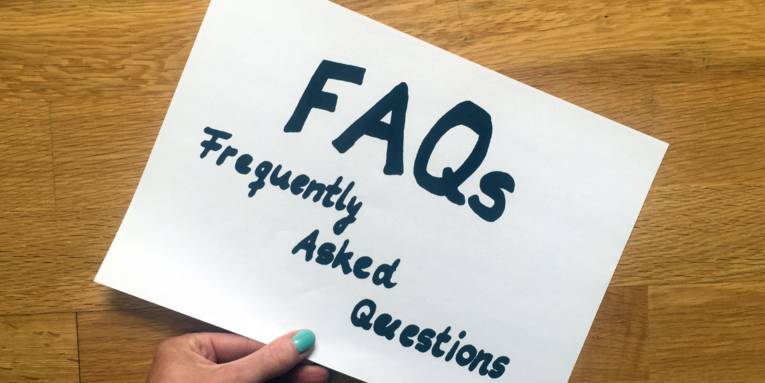 Eine Hand und ein Zettel, auf dem "FAQa - Frequently Asked Questions" steht.