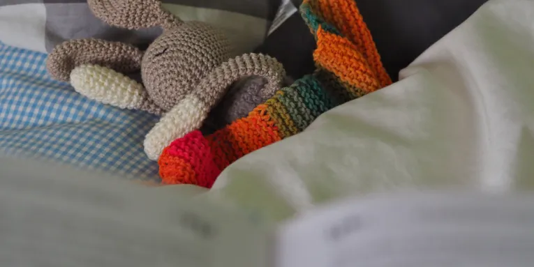 Blick über ein Buch auf ein Bett mit Kuscheltier.
