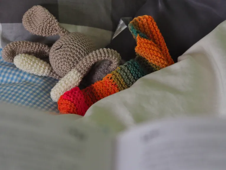 Blick über ein Buch auf ein Bett mit Kuscheltier.