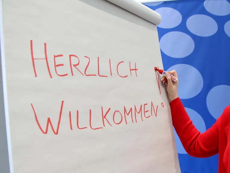 Auf ein Flipchart wird "Herzlich willkommen geschrieben"