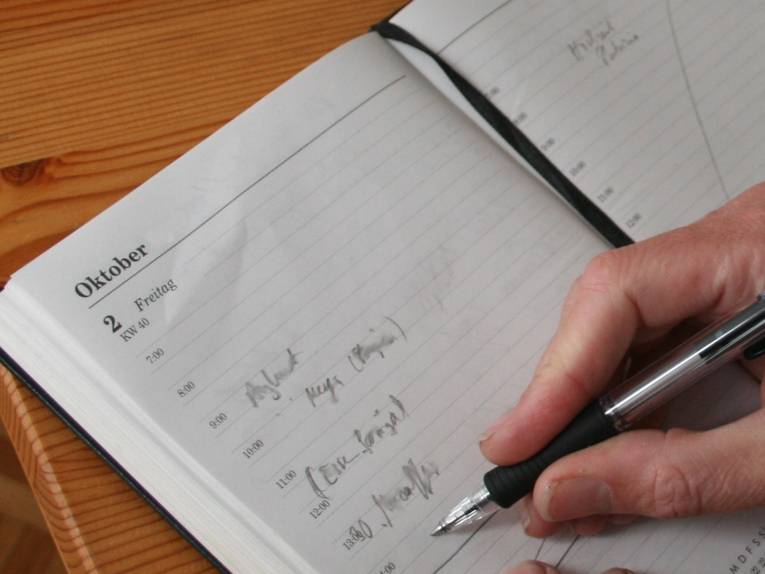 Eine Hand schreibt mit einem Kugelschreiber in einen Kalender.