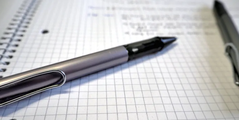 Ein Kugelschreiber liegt auf einem Schreibblock mit kariertem Papier. Handschriftliche Notizen stehen auf dem Papier.