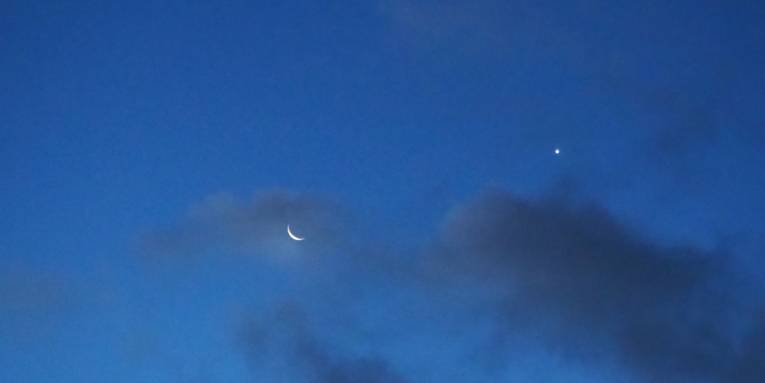 Abendhimmel mit Mond, einem Stern und dunklen Wolken.