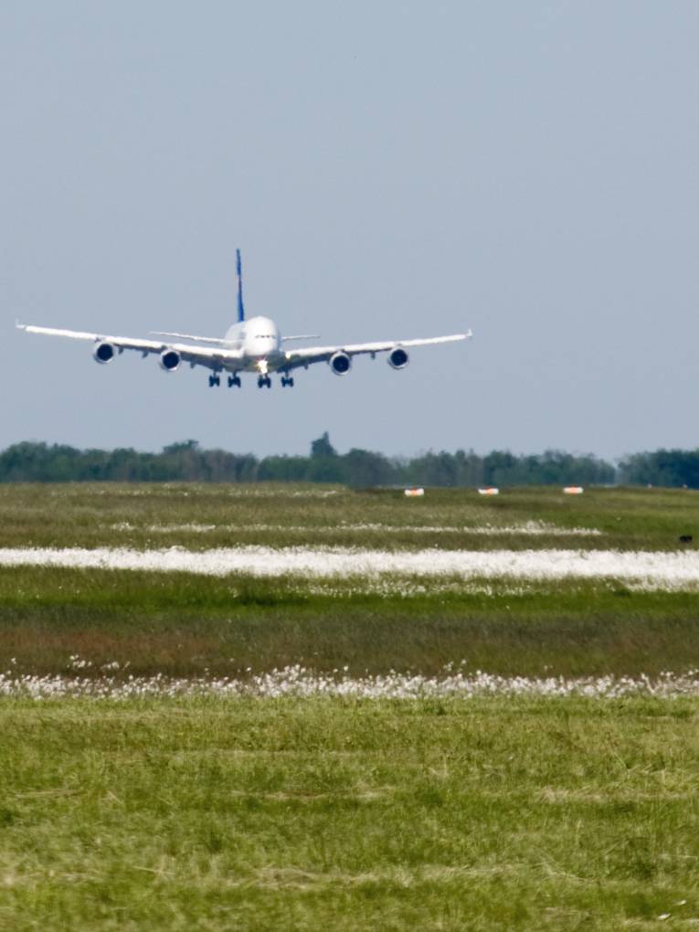 Ein Flugzeug hat Fahrwerk und Landeklappen ausgefahren und fliegt auf die Landebahn zu.