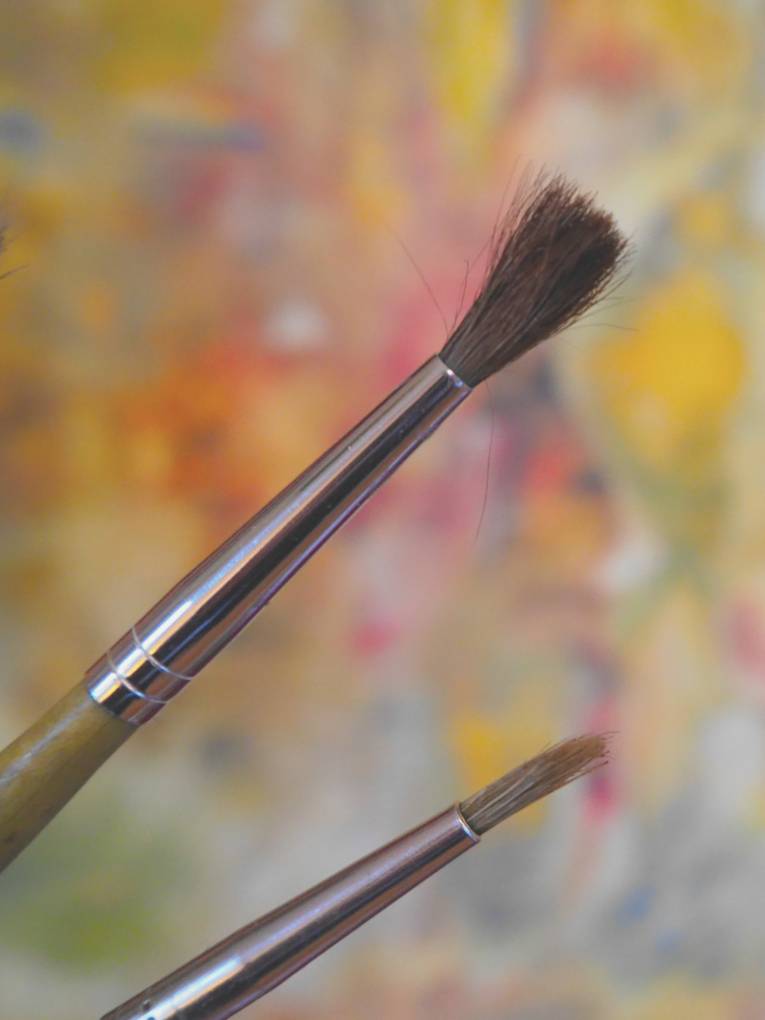 Verschiedene Pinsel vor einem farbigen Hintergrund.