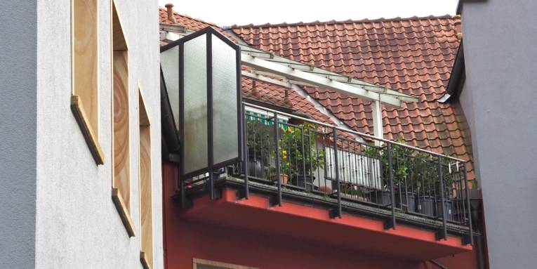 Blick von unten auf einen Balkon im Dachgeschoss, die Hausfassade ist rot.