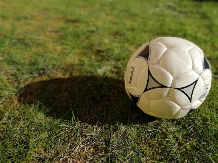 Ein Fußball, der auf einem Rasen liegt und einen Schatten wirft.