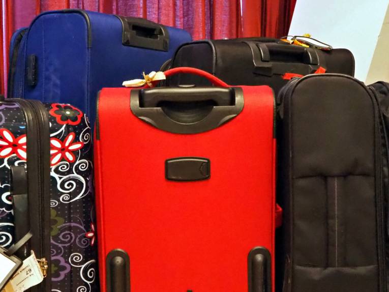 Um einen roten Koffer stehen weitere Koffer in verschiedenen Farben und einer mit einem floralen Muster.