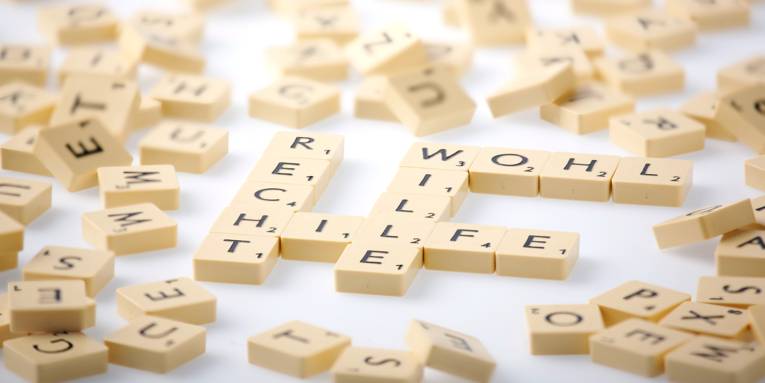 Spielsteine sind auf einem Tisch zu den Worten "Recht, "Wohl", "Wille" und "Hilfe" gelegt. Drumherum liegen weitere Spielsteine durcheinander.