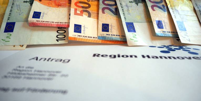 Geldscheine hängen nebeneinander, darunter ist ein Antragsformular der Region Hannover für Fördergeld.
