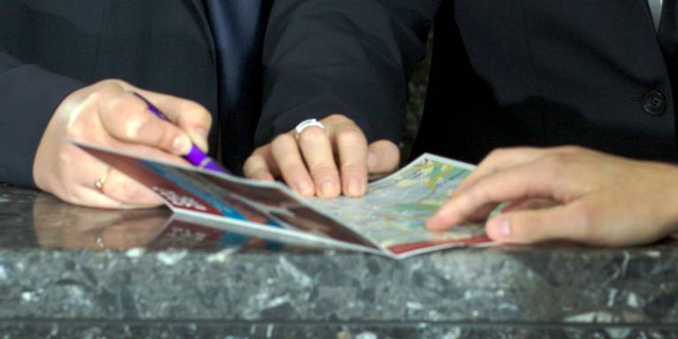 Eine Broschüre liegt auf einem Tresen, die Hände mehrerer Personen berühren die aufgeschlagenen Seiten.