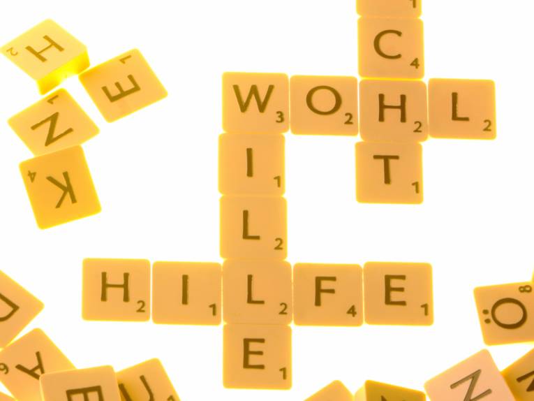Buchstabenbausteine bilden Worte wie "Wohl, Wille, Hilfe, weitere Buchstaben liegen daneben.